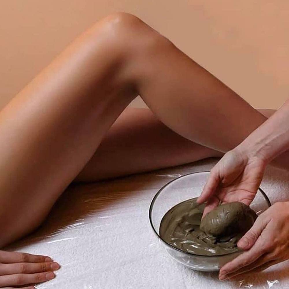 Woman applying GUAM seaweed mud to her legs from a bowl before a thigh wrap for weight loss