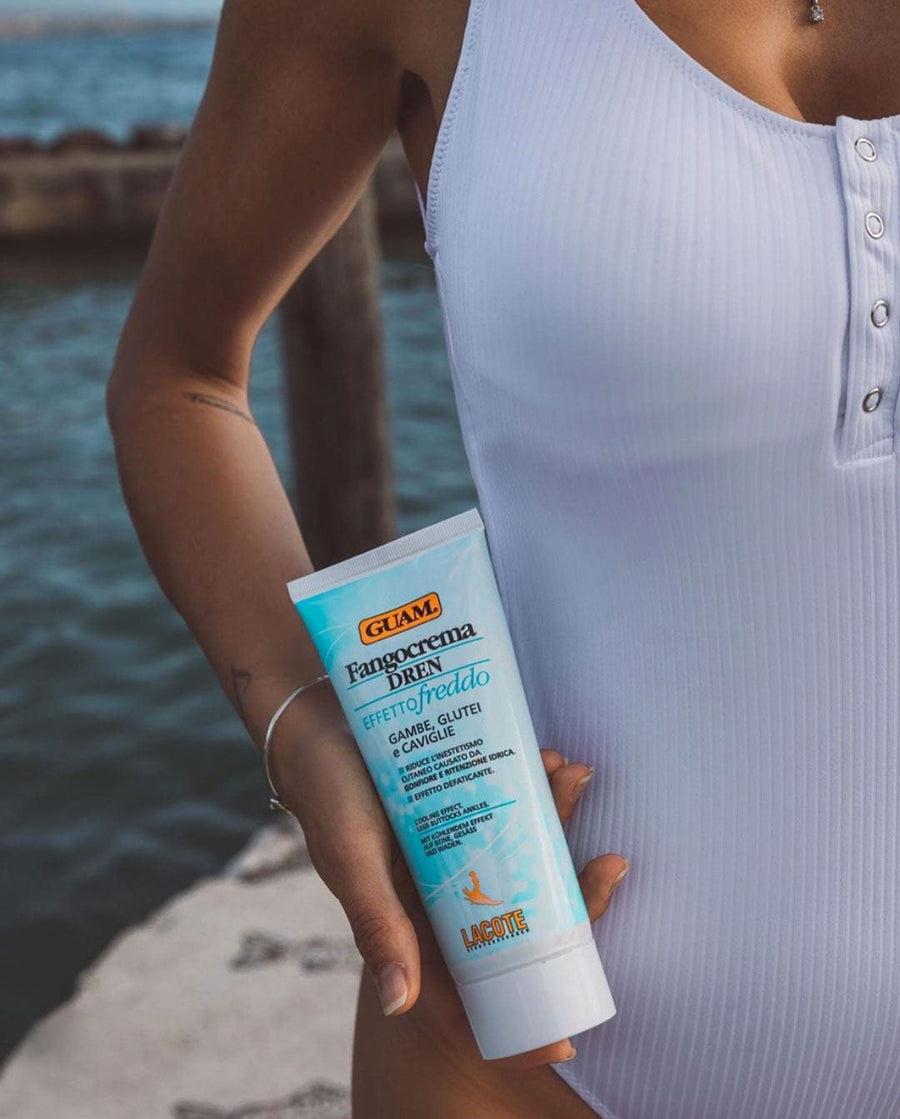 Woman holding a GUAM Dren cream tube by the pool, treating water retention in her thighs