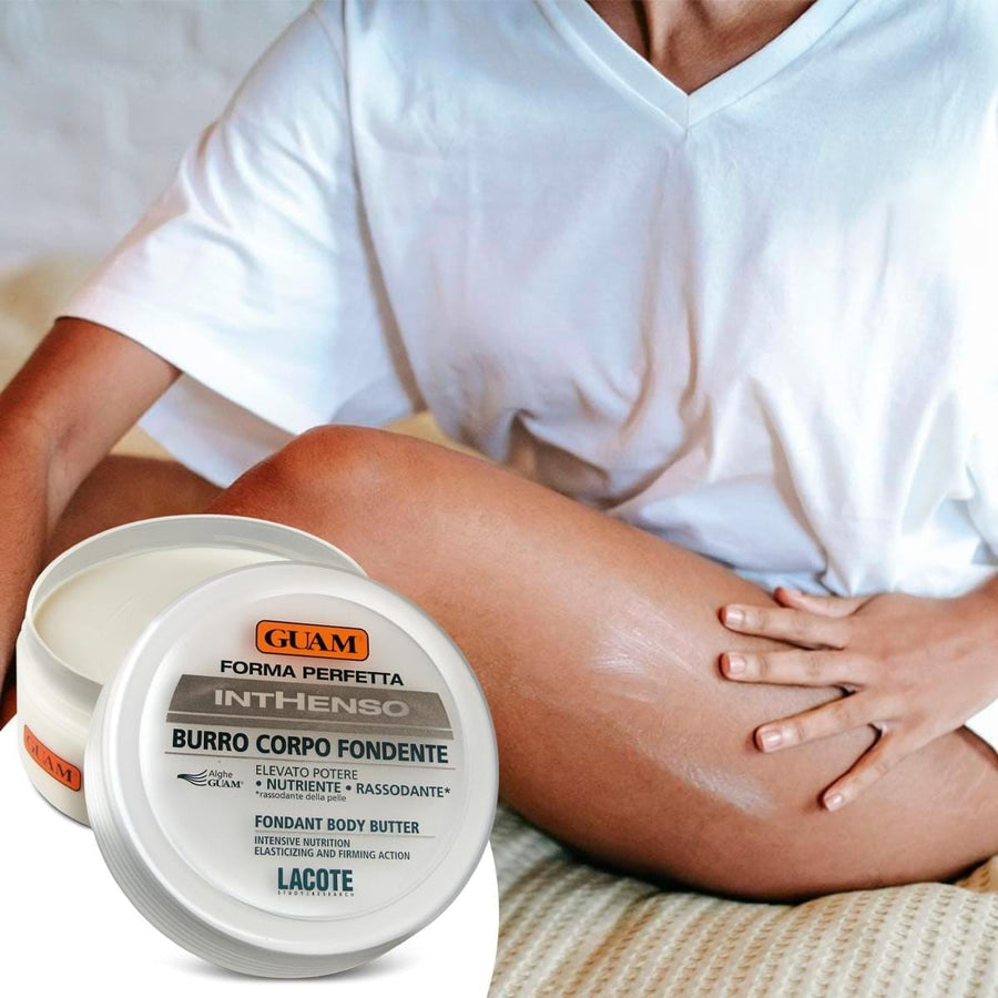Woman sitting on a bed massaging GUAM cellulite cream from a jar into her leg
