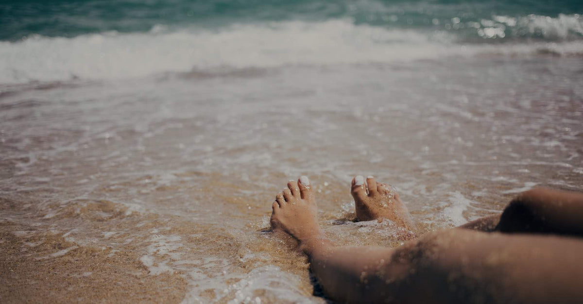 Feet in sea foam at the shore, the marine origin of a seaweed body wrap treatment