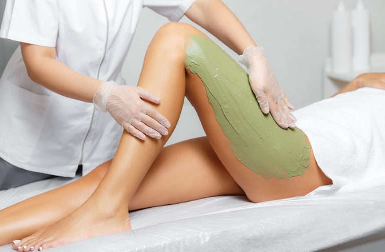 Spa therapist applying green seaweed mud to a client's leg during a spa body wrap treatment