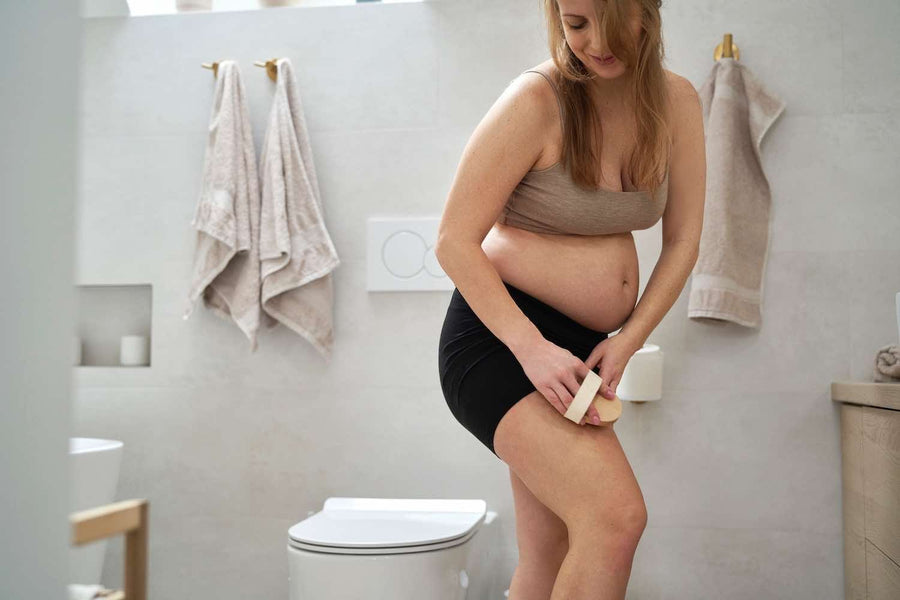 Woman applying seaweed mud to her thighs in the bathroom before wrapping them for an at-home body wrap