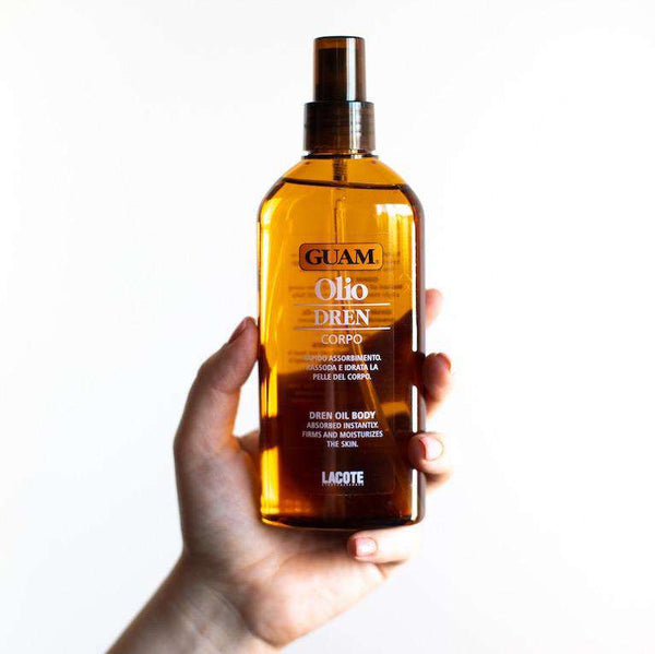 Hand holding GUAM Dren draining body oil for a firming leg massage