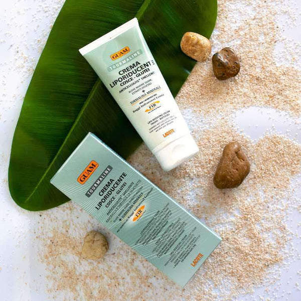 GUAM Extra Slimming Lipo Cream tube and box on sand, a fat burning cream for thighs and buttocks