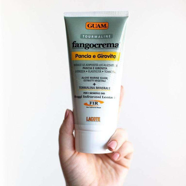 Hand holding GUAM Tummy Tightening Cream, a skin tightening cream for stomach cellulite with infrared heat